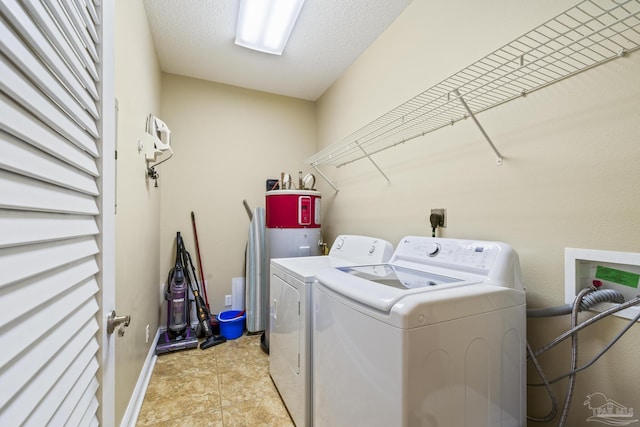 clothes washing area featuring laundry area, light tile patterned floors, baseboards, a textured ceiling, and separate washer and dryer