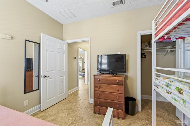 bedroom featuring light tile patterned floors, baseboards, visible vents, a textured ceiling, and a closet