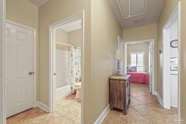 hall with attic access, visible vents, baseboards, and light tile patterned floors