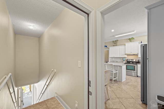 hall with a textured ceiling, light tile patterned flooring, an upstairs landing, and baseboards