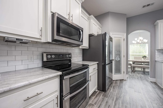 9074 Byrom Campbell Rd, Pace, FL 32571 - kitchen featuring stainless steel appliances, a chandelier, white cabinetry, wood finished floors, and decorative backsplash