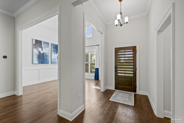 foyer entrance featuring dark wood-style flooring, a notable chandelier, crown molding, and baseboards