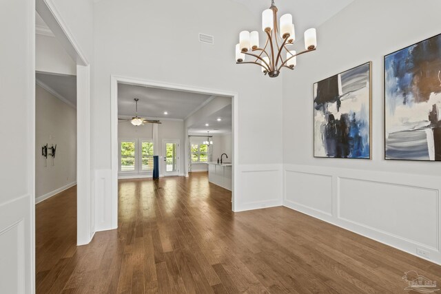 unfurnished dining area featuring ceiling fan with notable chandelier, wood finished floors, a sink, and ornamental molding