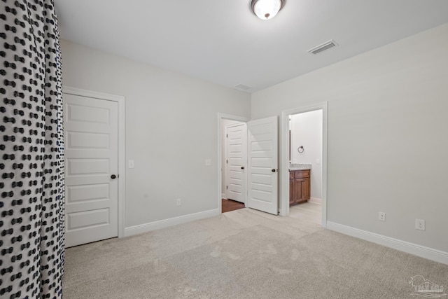 unfurnished bedroom with ensuite bath, visible vents, baseboards, and light carpet