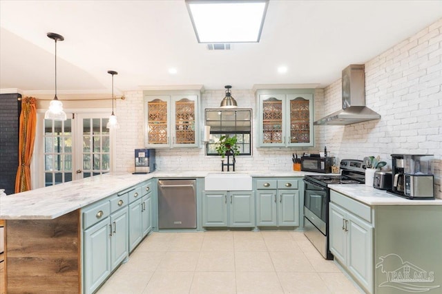 kitchen with kitchen peninsula, appliances with stainless steel finishes, wall chimney exhaust hood, sink, and hanging light fixtures