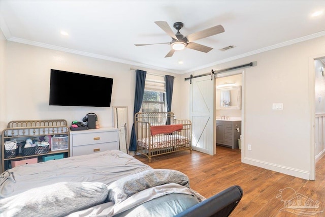 bedroom featuring connected bathroom, ceiling fan, a barn door, light hardwood / wood-style floors, and ornamental molding