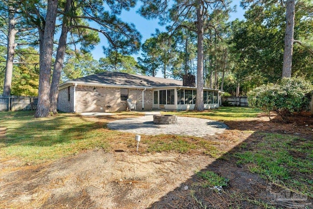 rear view of property featuring a lawn, a sunroom, a patio area, and an outdoor fire pit