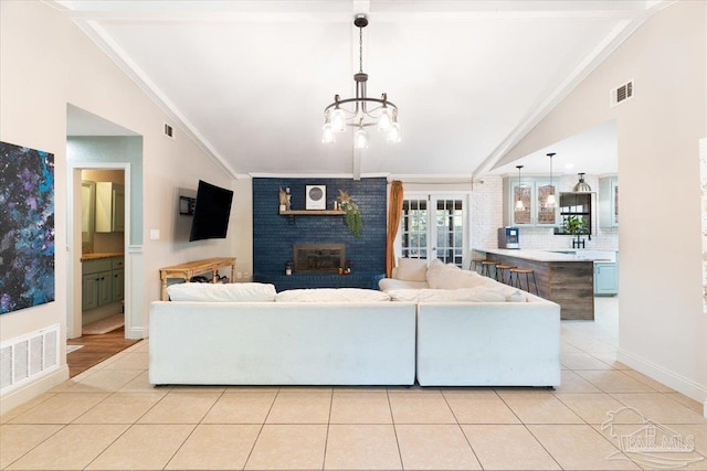 tiled living room featuring vaulted ceiling, crown molding, sink, a notable chandelier, and a fireplace