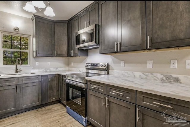 kitchen with dark brown cabinetry, stainless steel appliances, sink, light hardwood / wood-style floors, and hanging light fixtures