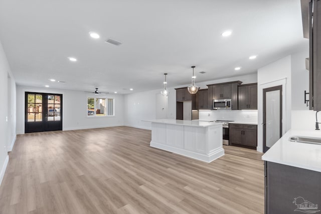 kitchen featuring backsplash, stainless steel appliances, light wood-type flooring, a center island, and ceiling fan