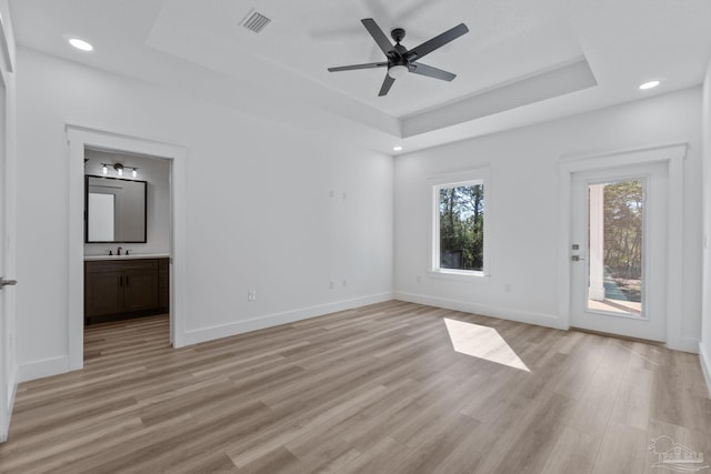 unfurnished bedroom featuring ceiling fan, a raised ceiling, light hardwood / wood-style floors, sink, and ensuite bathroom