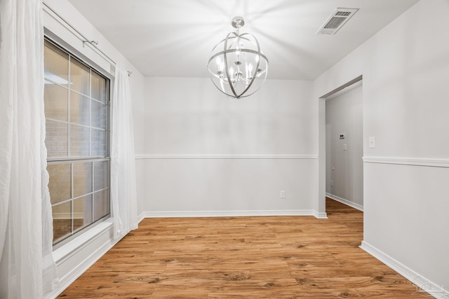 unfurnished dining area with visible vents, light wood-style flooring, baseboards, and an inviting chandelier