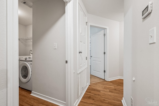 clothes washing area with washer / clothes dryer, visible vents, wood finished floors, laundry area, and baseboards