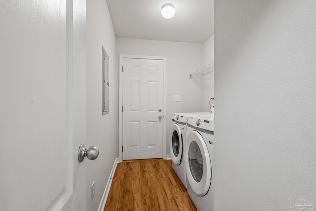 clothes washing area featuring laundry area, electric panel, baseboards, light wood-style flooring, and washing machine and clothes dryer