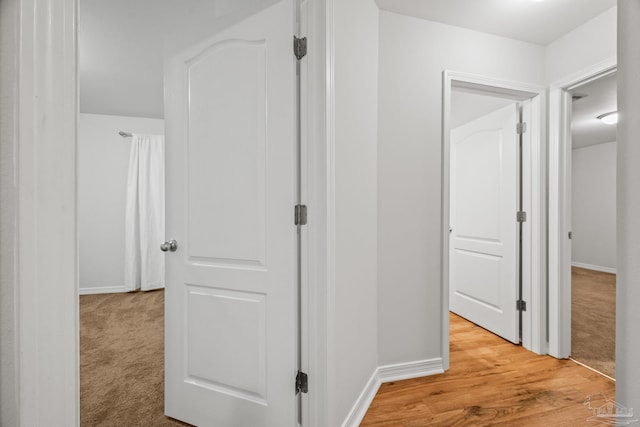 corridor with light carpet, light wood-style flooring, and baseboards