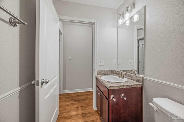 half bathroom with vanity, wood finished floors, and toilet