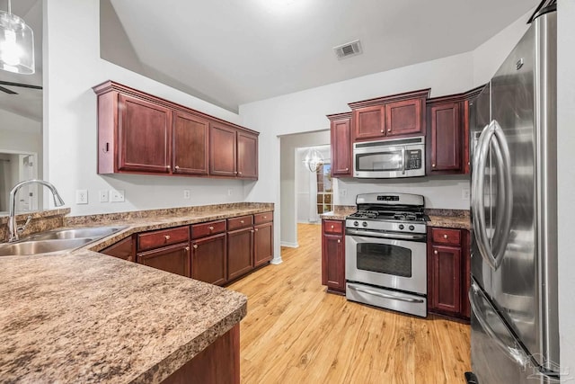 kitchen with reddish brown cabinets, visible vents, light wood-style flooring, stainless steel appliances, and a sink