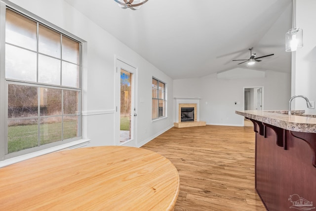 interior space featuring light wood-style floors, vaulted ceiling, ceiling fan, a tile fireplace, and baseboards