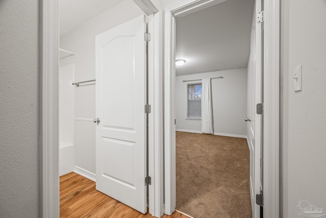 hallway featuring light carpet, light wood-type flooring, and baseboards