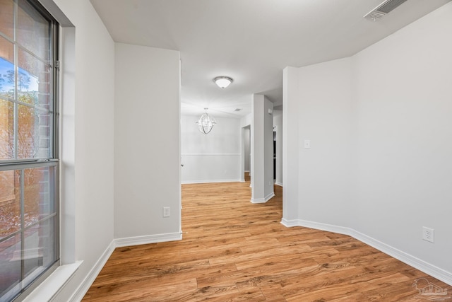 empty room featuring light wood-style floors, baseboards, visible vents, and a notable chandelier