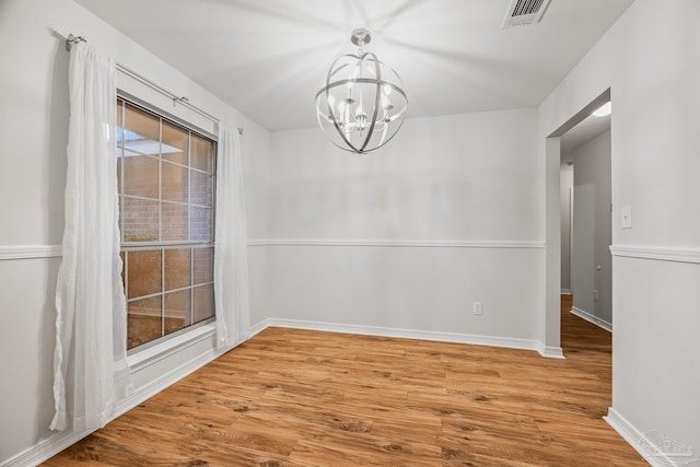 empty room with a notable chandelier, baseboards, visible vents, and wood finished floors