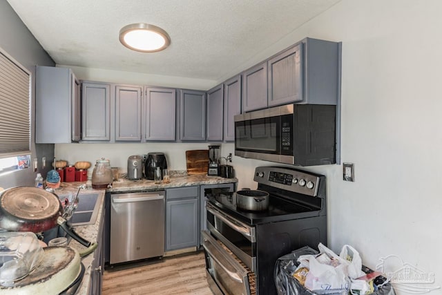 kitchen with stainless steel appliances, a textured ceiling, light stone countertops, and gray cabinetry