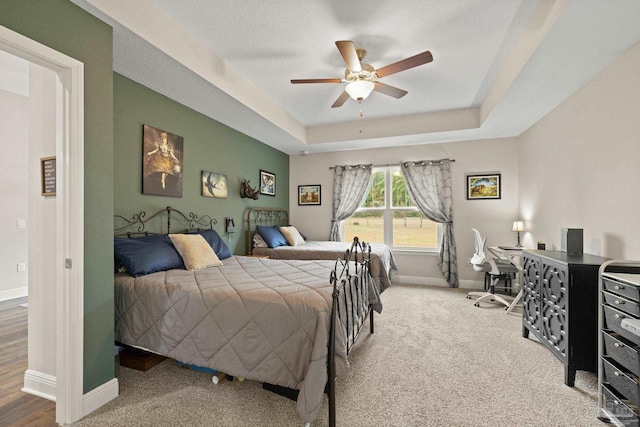 bedroom with ceiling fan, carpet floors, a textured ceiling, and a tray ceiling