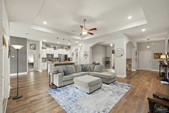 living room featuring a tray ceiling, ceiling fan, and dark wood-type flooring