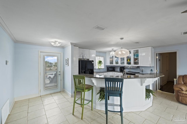 kitchen featuring a breakfast bar, white cabinetry, black fridge, hanging light fixtures, and kitchen peninsula