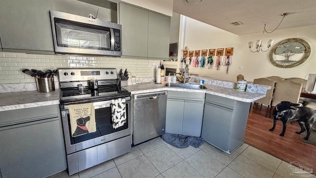 kitchen featuring light tile patterned flooring, sink, appliances with stainless steel finishes, kitchen peninsula, and backsplash