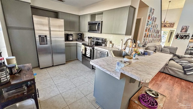 kitchen with sink, gray cabinetry, stainless steel appliances, a kitchen bar, and kitchen peninsula