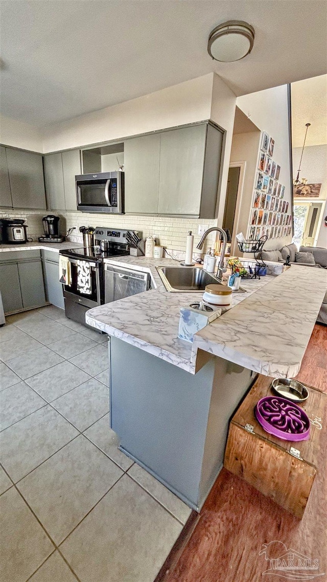 kitchen with sink, light tile patterned floors, stainless steel appliances, decorative backsplash, and kitchen peninsula