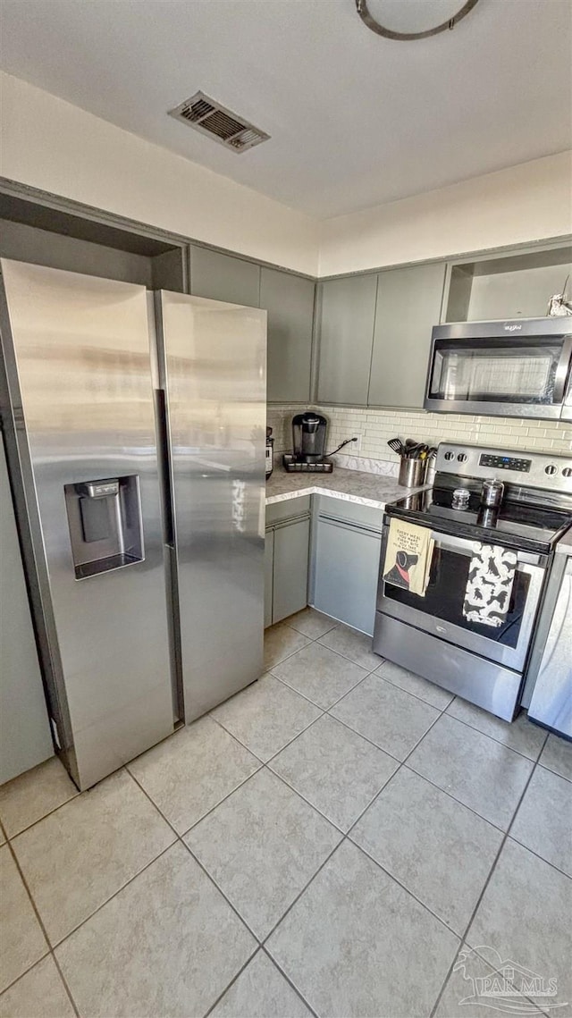 kitchen with stainless steel appliances, gray cabinets, light tile patterned floors, and backsplash