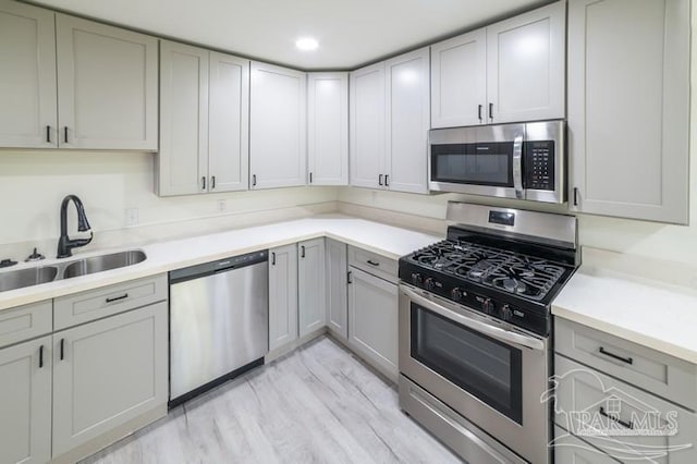 kitchen with gray cabinets, light countertops, light wood-style floors, stainless steel appliances, and a sink