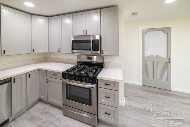 kitchen featuring light countertops, appliances with stainless steel finishes, gray cabinetry, and light wood-style floors