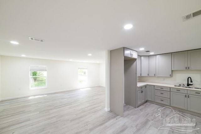 kitchen with visible vents, a sink, open floor plan, light wood-style floors, and gray cabinets