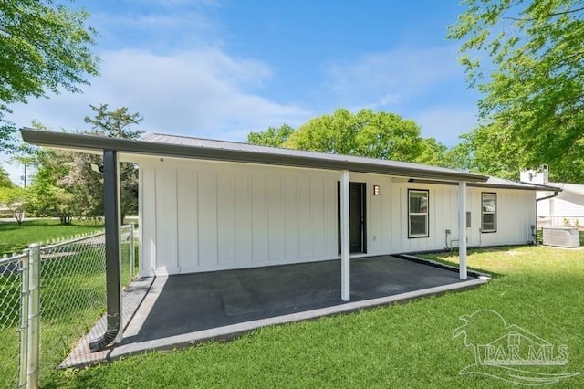 back of house featuring cooling unit, board and batten siding, fence, and a lawn