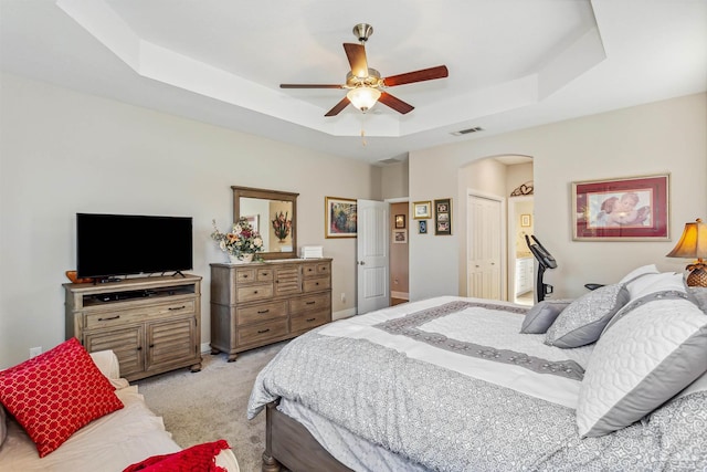 bedroom featuring ceiling fan, light carpet, a tray ceiling, and a closet