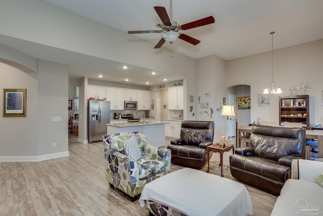 living room featuring ceiling fan with notable chandelier, light hardwood / wood-style flooring, sink, and high vaulted ceiling