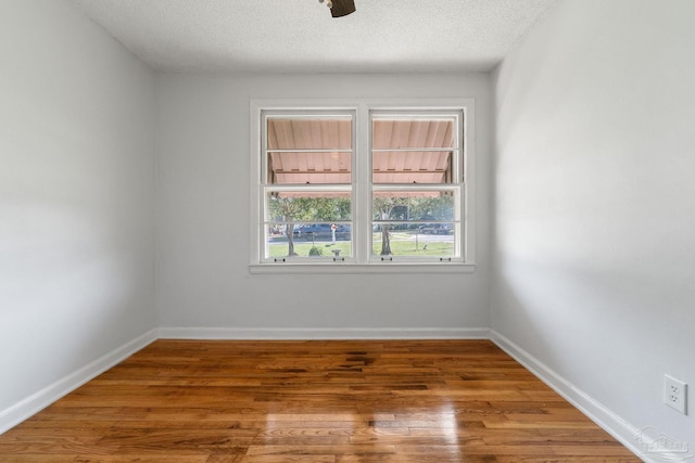 unfurnished room with a textured ceiling, baseboards, and wood finished floors