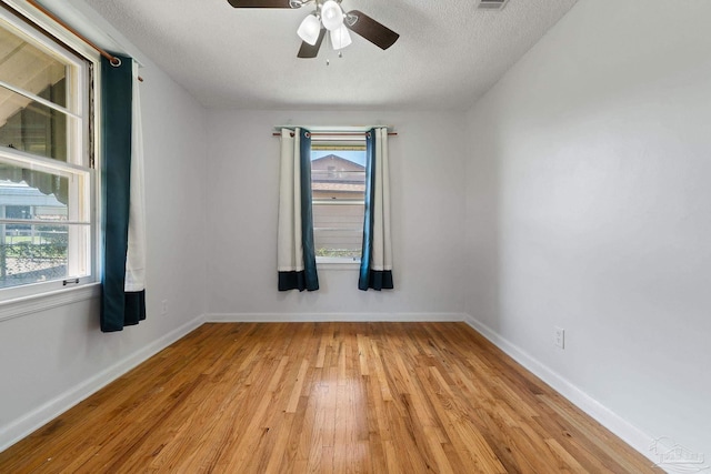 empty room with a textured ceiling, light wood-style flooring, a ceiling fan, visible vents, and baseboards