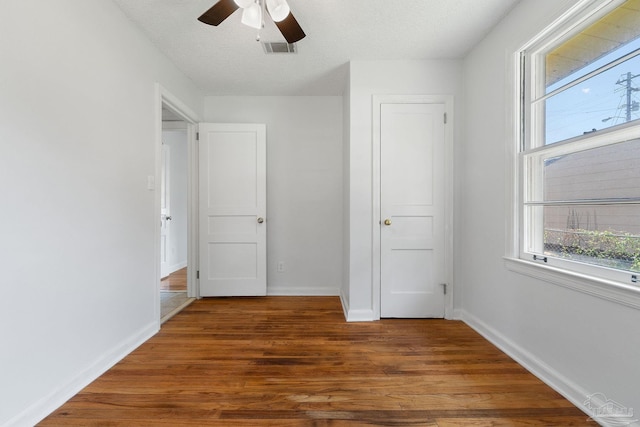 unfurnished bedroom with a textured ceiling, dark wood-style flooring, a ceiling fan, visible vents, and baseboards