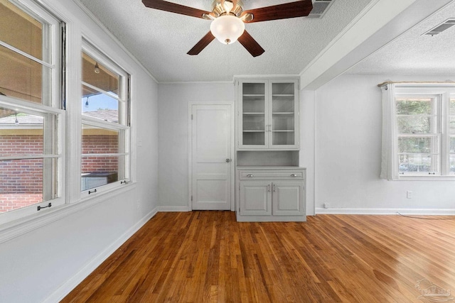 unfurnished room featuring a textured ceiling, dark wood finished floors, visible vents, and a healthy amount of sunlight