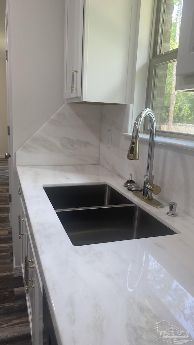details featuring white cabinets, light stone countertops, a sink, dark wood-type flooring, and backsplash
