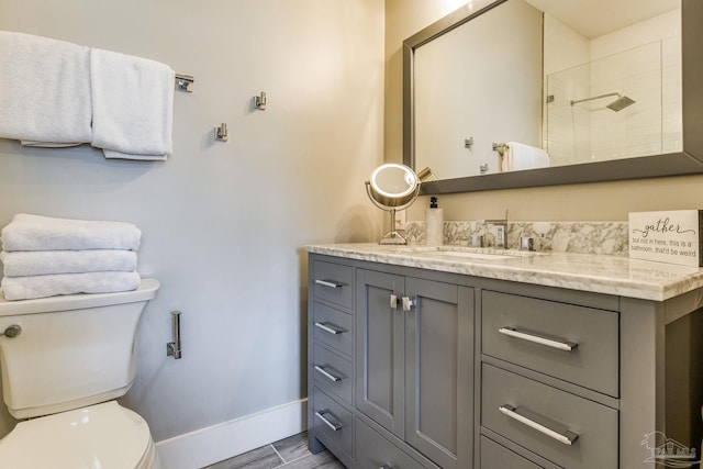 full bath featuring vanity, wood finished floors, baseboards, a tile shower, and toilet