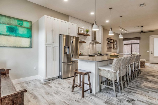 kitchen with visible vents, open shelves, stainless steel fridge, light wood-style floors, and wall chimney exhaust hood