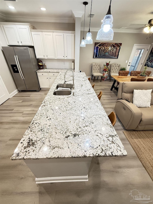 kitchen featuring hanging light fixtures, stainless steel refrigerator with ice dispenser, a kitchen bar, white cabinetry, and sink