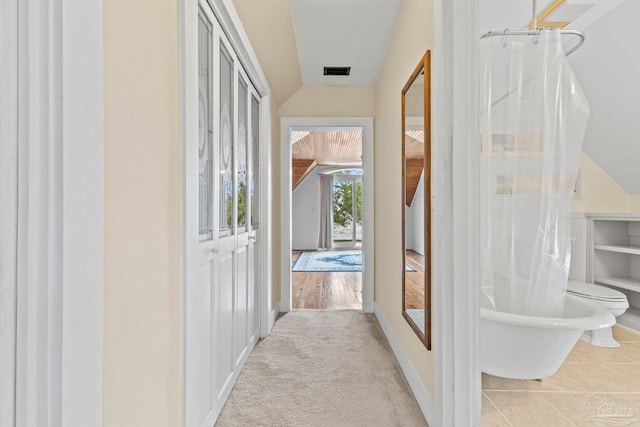 hallway with visible vents, vaulted ceiling, and carpet floors