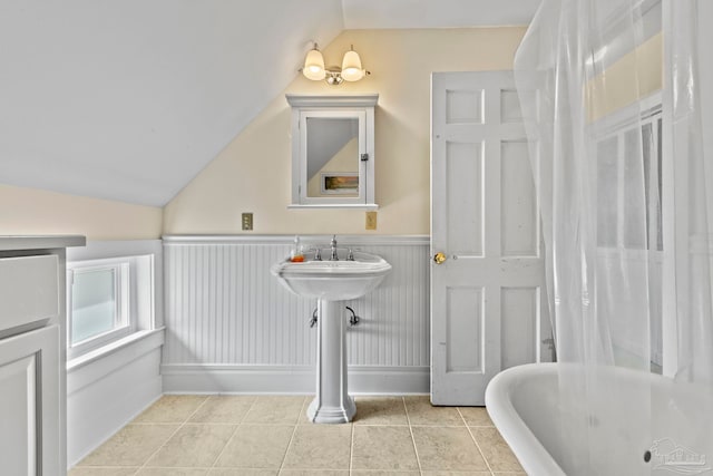bathroom featuring tile patterned floors, a wainscoted wall, a bathing tub, and lofted ceiling