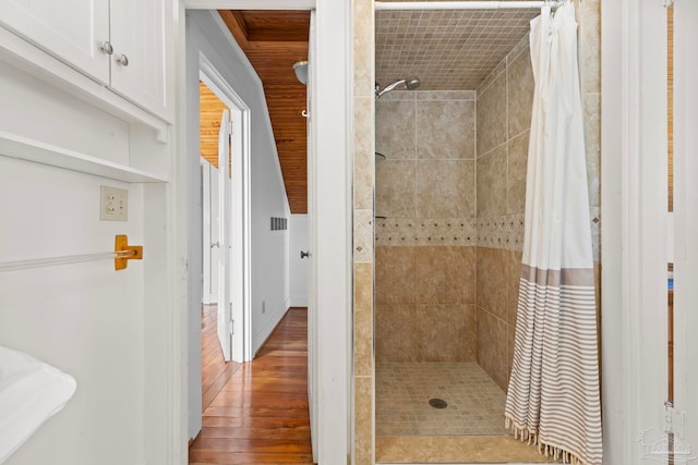 bathroom with wood finished floors, a tile shower, and visible vents
